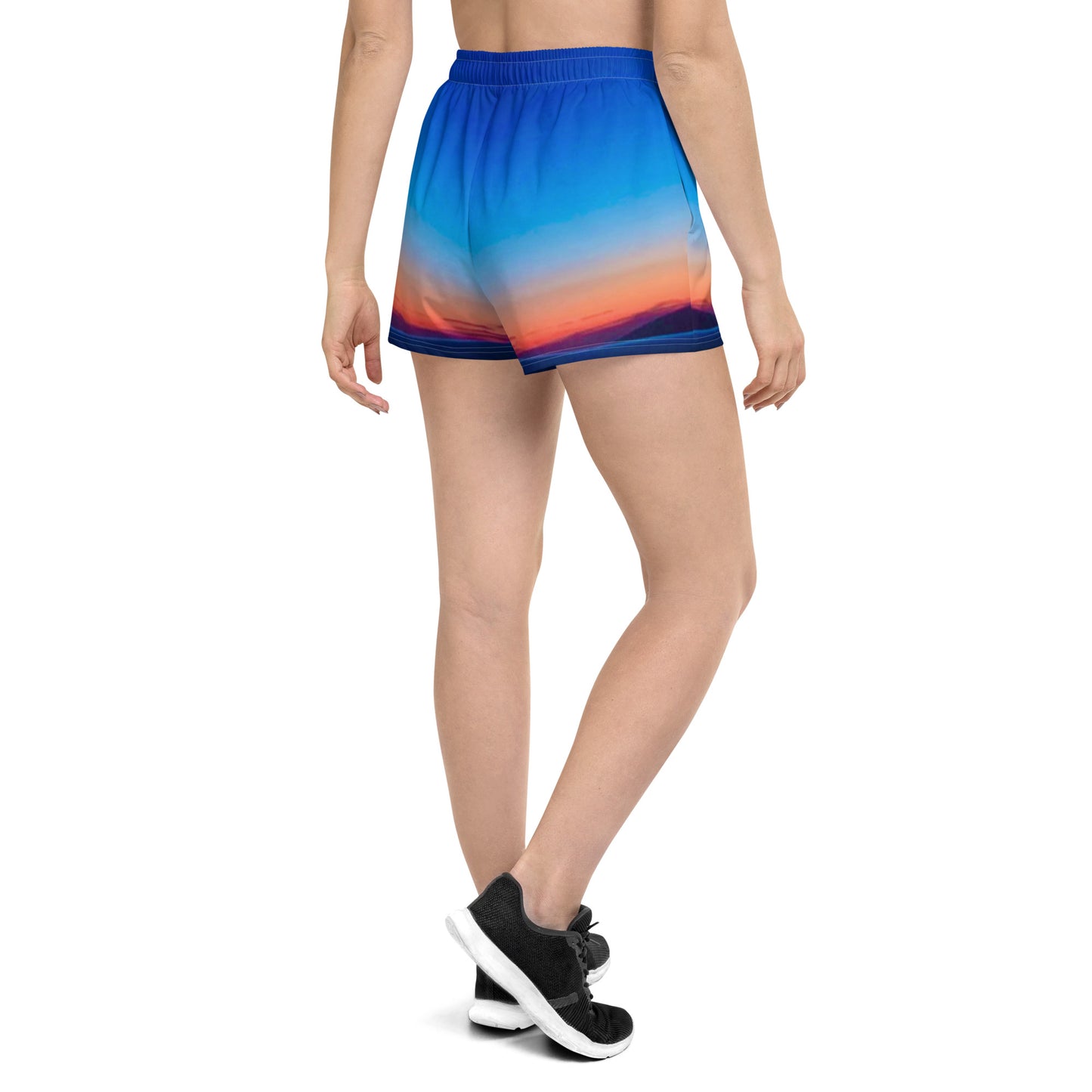 Back view of woman wearing kallistii skyline print running shorts in blue and orange gradient with black athletic shoes