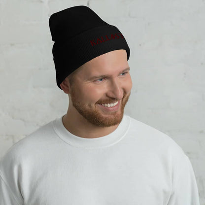 Smiling man wearing black KALLISTII embroidered beanie and white sweatshirt against light background