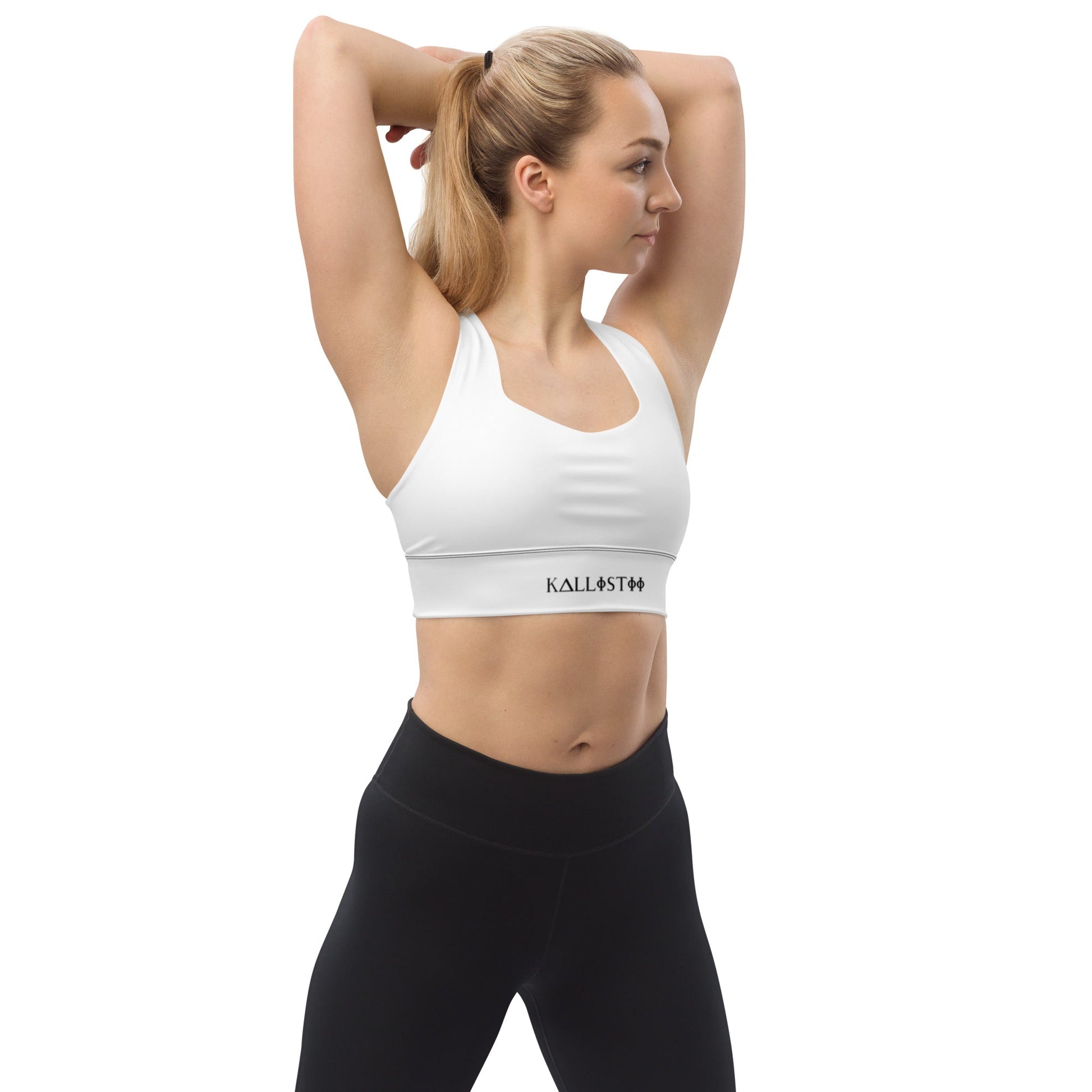 Woman wearing white KALLISTII activewear sports bra and black leggings stretching with arms raised