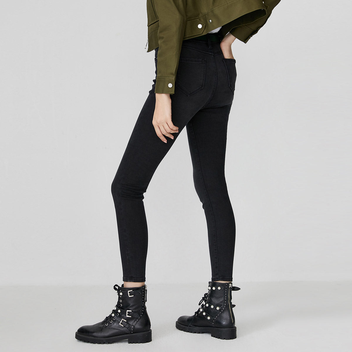 Woman wearing kallistii black fade skinny jeans paired with black studded combat boots and green jacket